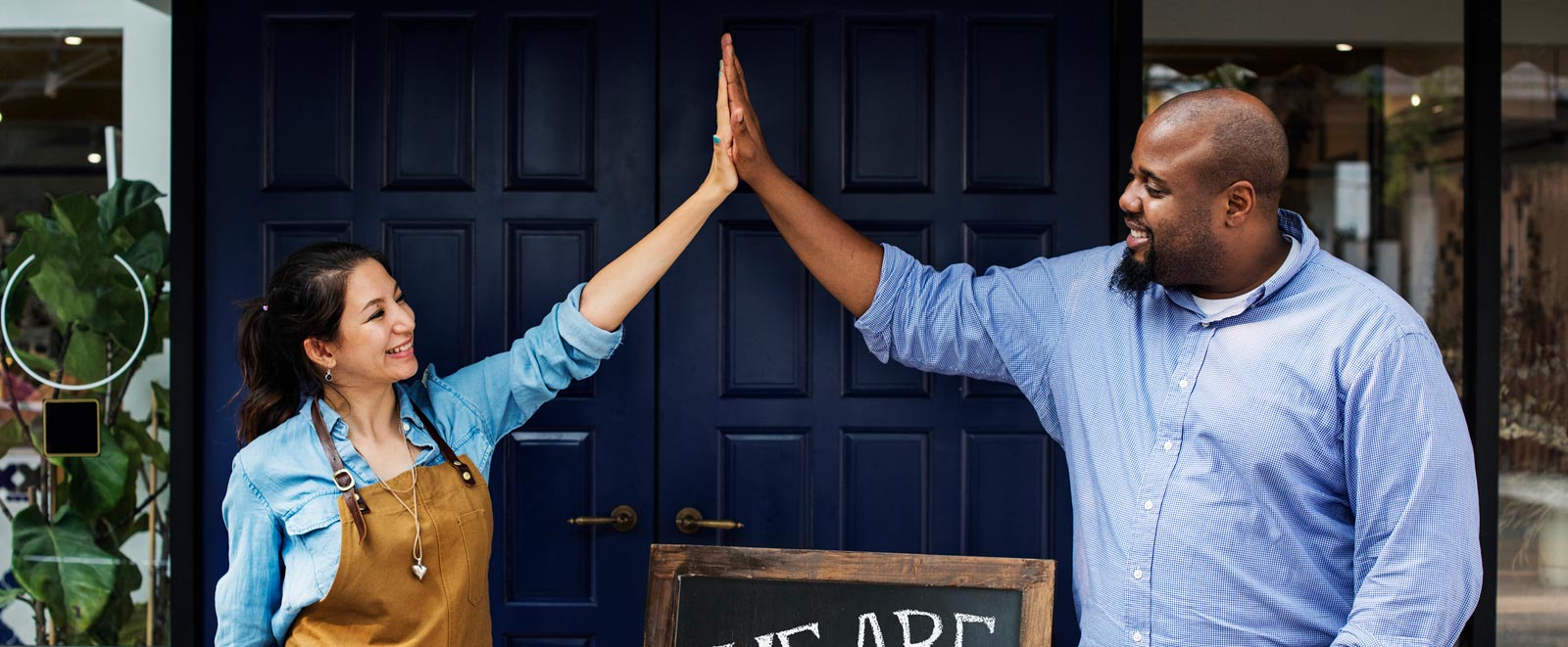 Two business owners high-fiving outside their shop